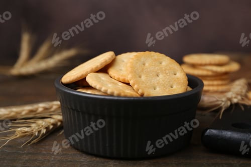 Preview: Tasty salty crackers and wheat spikes on wooden table, closeup