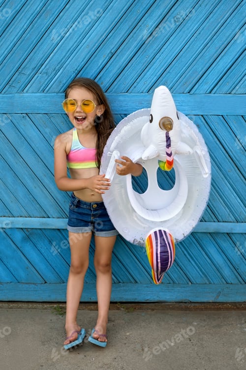 Preview: Girl with a unicorn-shaped swimming circle in her hands against a blue wall