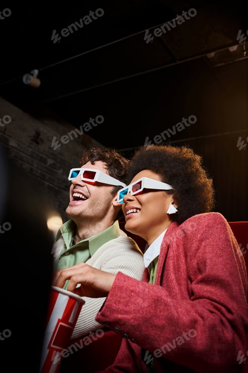 Preview: jolly diverse couple with retro 3d glasses enjoying movie at cinema on date on Valentines day