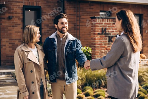 Preview: Happy smiling couple shaking hands with realtor after buying new home