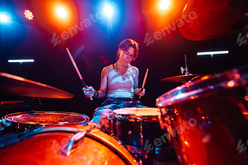 Preview: Female drummer performing energetically on stage under colorful lights