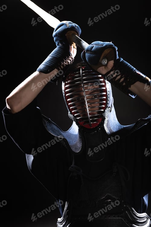 Preview: Kendo fighter in armor practicing with bamboo sword and looking at camera on black
