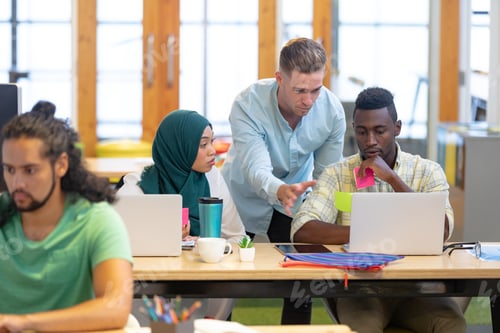 Preview: Front view of diverse business people working together on laptop at desk in a modern office