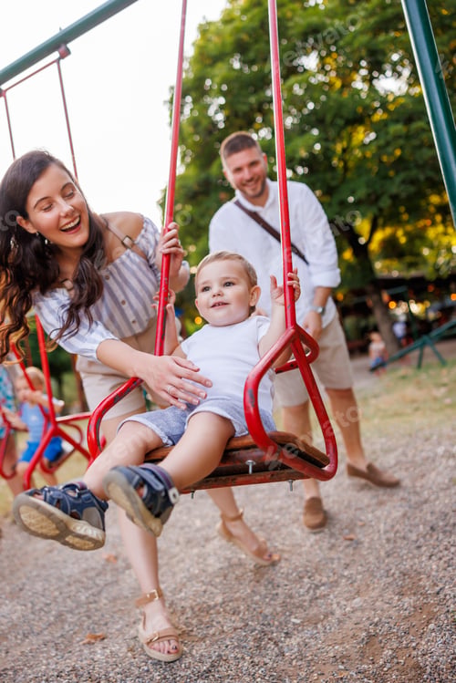 Preview: Parents playing with toddler son on a swing in the park