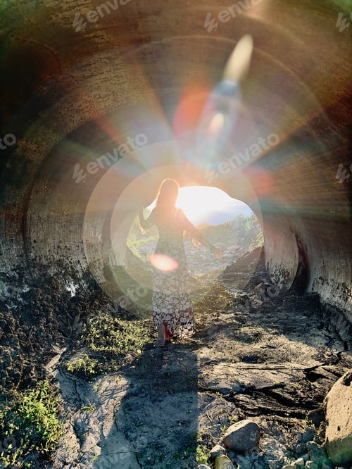Preview: a girl in a long dress is illuminated by the sun in a tunnel