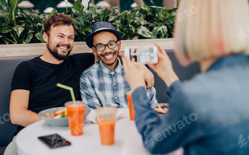 Preview: Woman taking photo of diverse friends in cafe