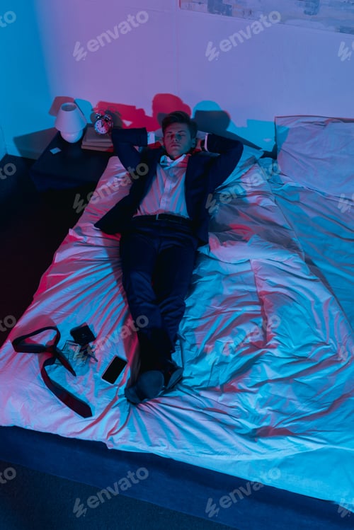 Preview: high angle view of tired young businessman relaxing in bed