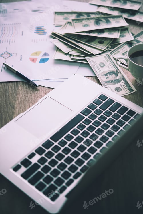 Preview: Working place of trader. The table covered by cash notes, keyboard and financial charts.