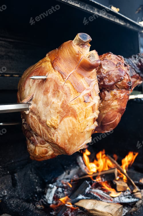 Preview: Pork leg are roasted on a spit on a grill outside.