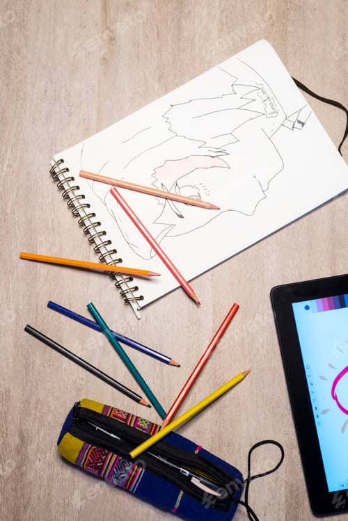 Preview: Above view of open exercise book, pencil crayons and tablet on white desk