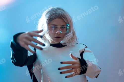 Preview: Woman looking through the illuminated futuristic glasses, virtual reality on a blue background