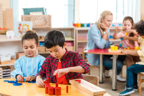Preview: Selective focus of kids playing games with children and teacher at background in montessori school