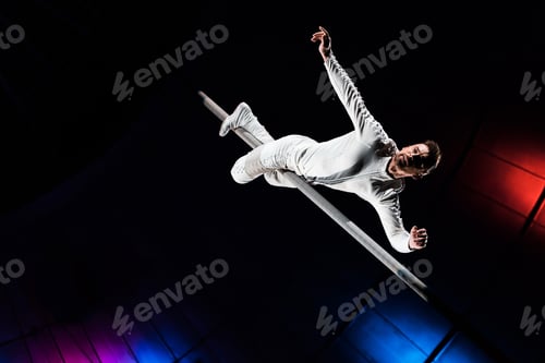 Vista previa: low angle view of handsome acrobat holding metallic pole with legs while performing in circus