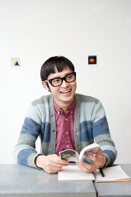 Preview: Young man enjoying a good book at a table with a joyful expression.