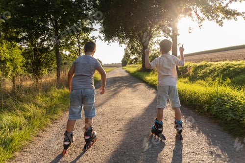 Preview: Two children skate happily along a dirt path surrounded by green trees and fields.