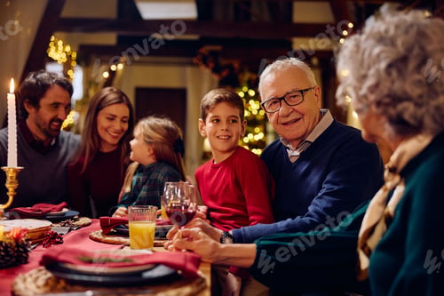 Preview: Happy senior man enjoying with his extended family at dining table at Christmas.