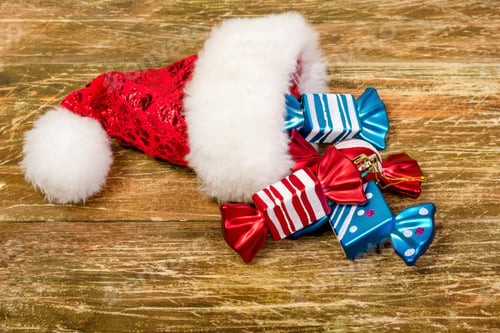 Preview: Santa's cap and colorful colored candy lay on a scratched wooden table.