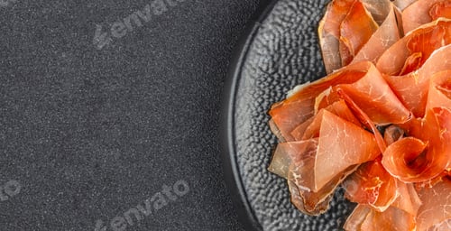 Preview: Overhead view of sliced cured ham on a black plate with copy space for gourmet food advertising