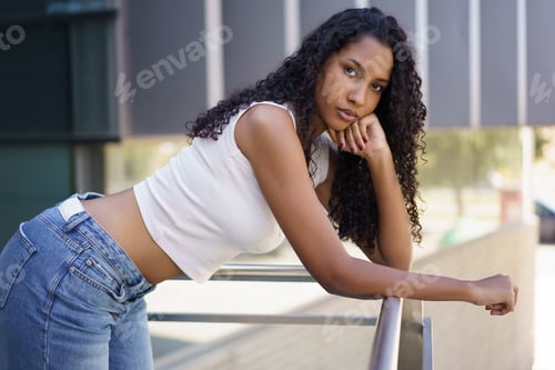 Preview: A Stylish Young Woman is Posing Outdoors with her Curly Hair in the Bright Sunlight