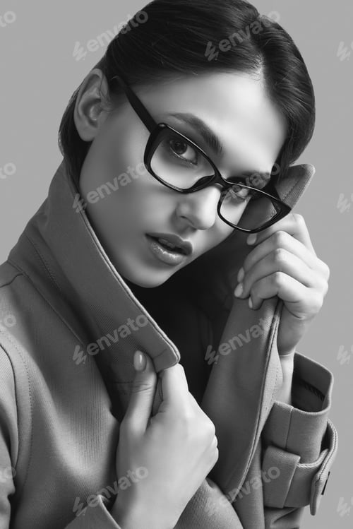 Preview: Portrait Of Young Beautiful Hipster Woman In Fashionable Coat And Eyeglasses Posing On Dark Grey