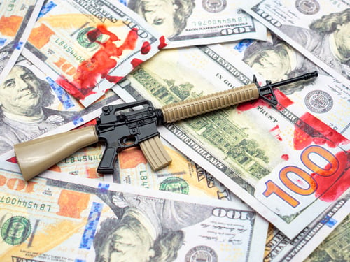Preview: Closeup shot of a toy rifle on dollar bills with red blood spots on them