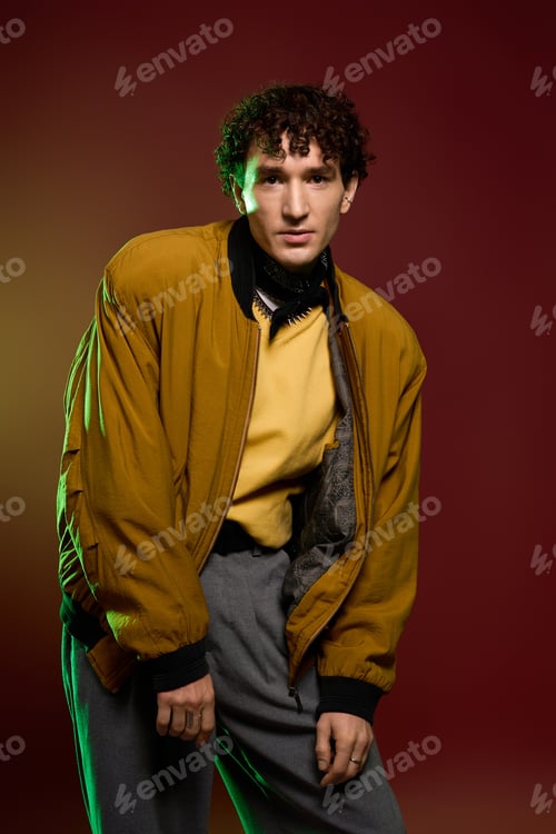 Preview: Stylish man showcases vibrant fashion in artistic urban background during evening shoot