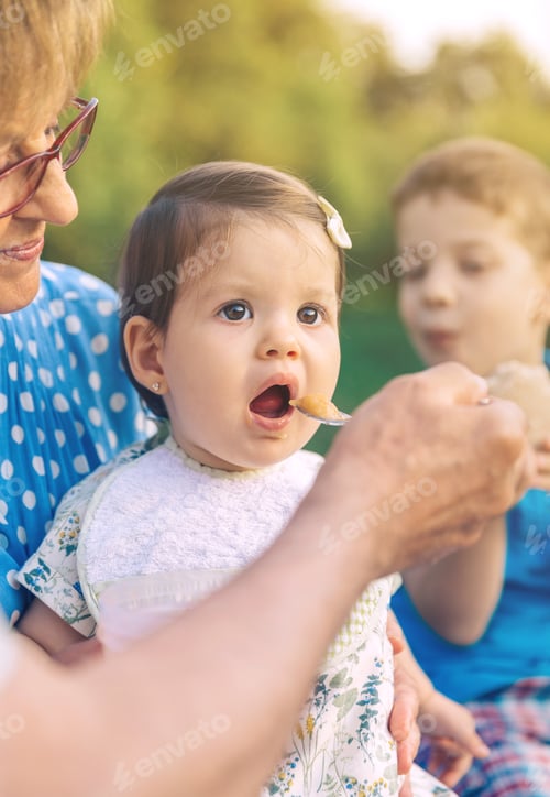 Preview: Senior man feeding to baby girl sitting in a bench