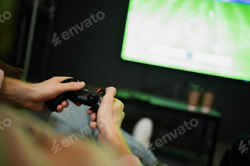 Preview: KYIV, UKRAINE - FEBRUARY 13, 2023: Cropped view of man playing video game near blurred tv in cyber