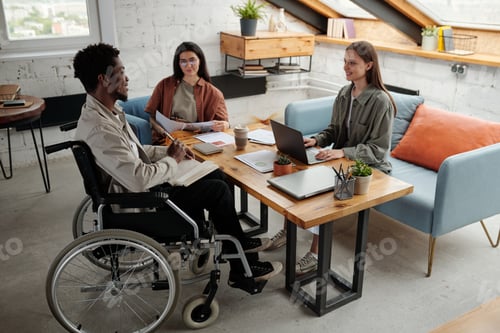 Preview: Two young female managers looking at confident male colleague in wheelchair