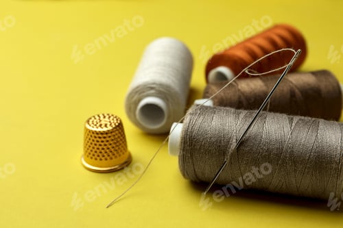 Preview: Different colorful sewing threads with needle and thimble on yellow background, closeup