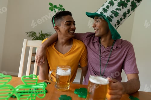 Preview: Smiling mixed race gay male couple wearing st patrick's day costumes embracing and holding beers