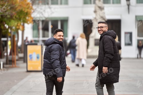 Preview: Two men looking at the camera and smiling while walking down the street together.