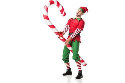 Preview: cheerful man in christmas elf costume riding big candy cane isolated on white