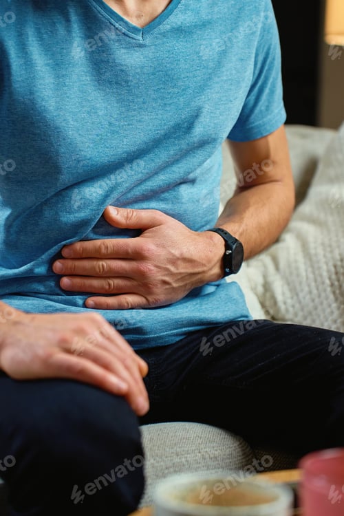 Preview: Man clutching his stomach, suffering from abdominal pain at home