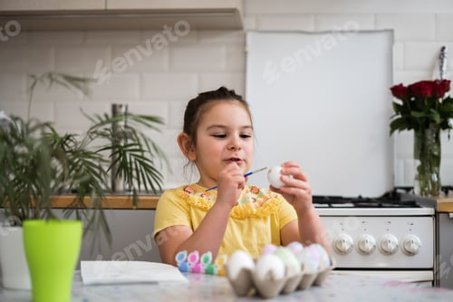 Preview: Child girl of preschool age painting Easter eggs at home kitchen. Easter spring traditions.