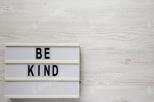 Preview: 'Be kind' on a lightbox on a white wooden background, top view.