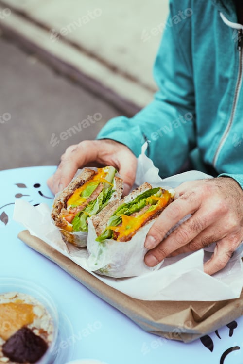 Preview: Man holding big portion sandwich outside closeup