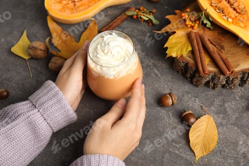Preview: Woman holding glass with pumpkin spice latte cream on table