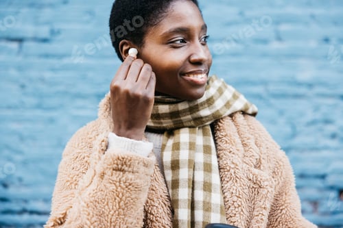Preview: Young woman wearing earbuds and smiling outdoors in winter
