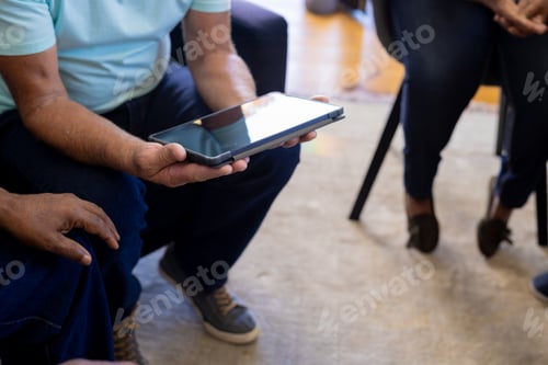 Preview: Mid section od senior diverse people sitting on chairs and using tablet in group therapy session