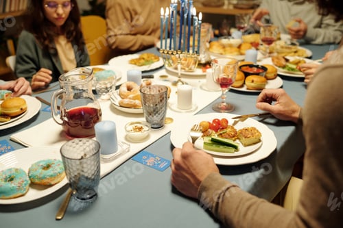 Preview: Hands of young Jewish man sitting by served table with snacks on his plate