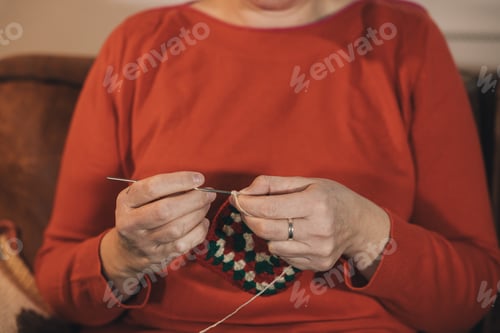 Preview: A woman is sitting on a couch and knitting, she is wearing a red sweater and a silver ring