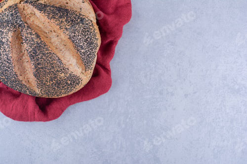 Preview: Red cloth under a loaf of black sesame coated bread on marble background