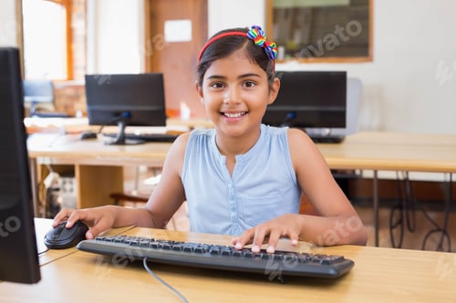 Preview: Indian schoolgirl wearing headband smiling at monitor in computer lab using keyboard and mouse