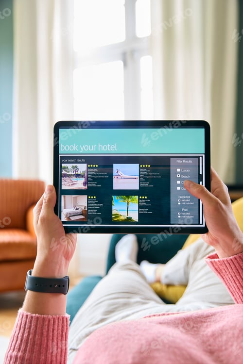 Preview: Close Up Of Woman Booking Holiday On Digital Tablet Lying On Sofa At Home