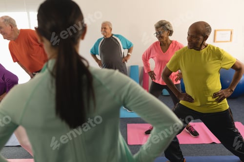 Preview: Rear view of young female trainer assisting a groupe of active senior people in fitness studio