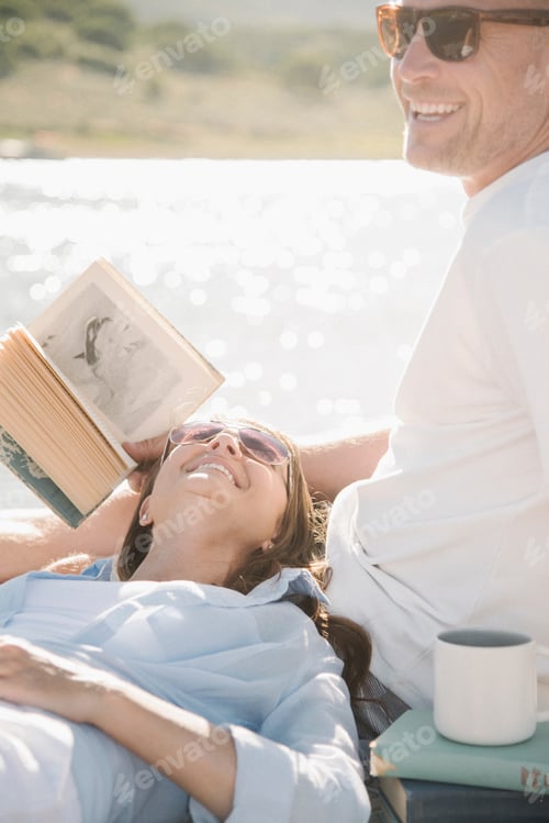 Preview: Man and woman reclining on a jetty, reading a book.