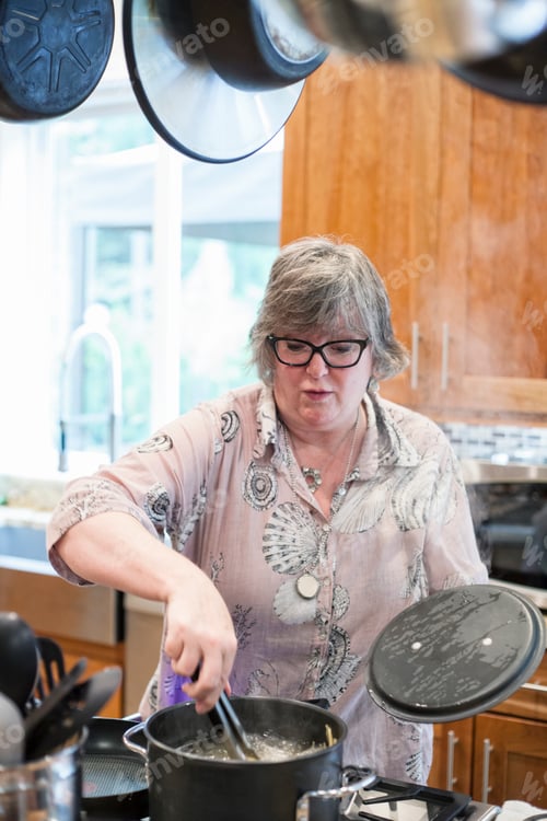 Preview: Senior woman checking to see if a pot of pasta is cooking correctly in a home kitchen.