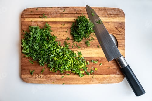 Preview: Freshly chopped herbs on a wooden cutting board with a chef's knife.