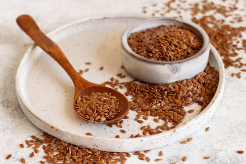 Preview: Raw Flax seeds in a ceramic plate with a wooden scoop